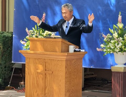 Man delivering a speech at a wooden podium outdoors.