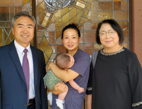 Three adults and a baby posing indoors with a stained glass backdrop.