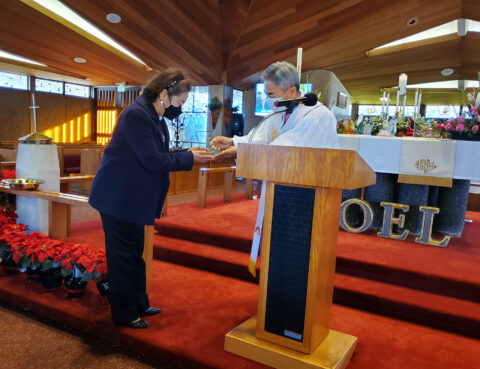 A woman receives a certificate from a man in a robe at a church podium.