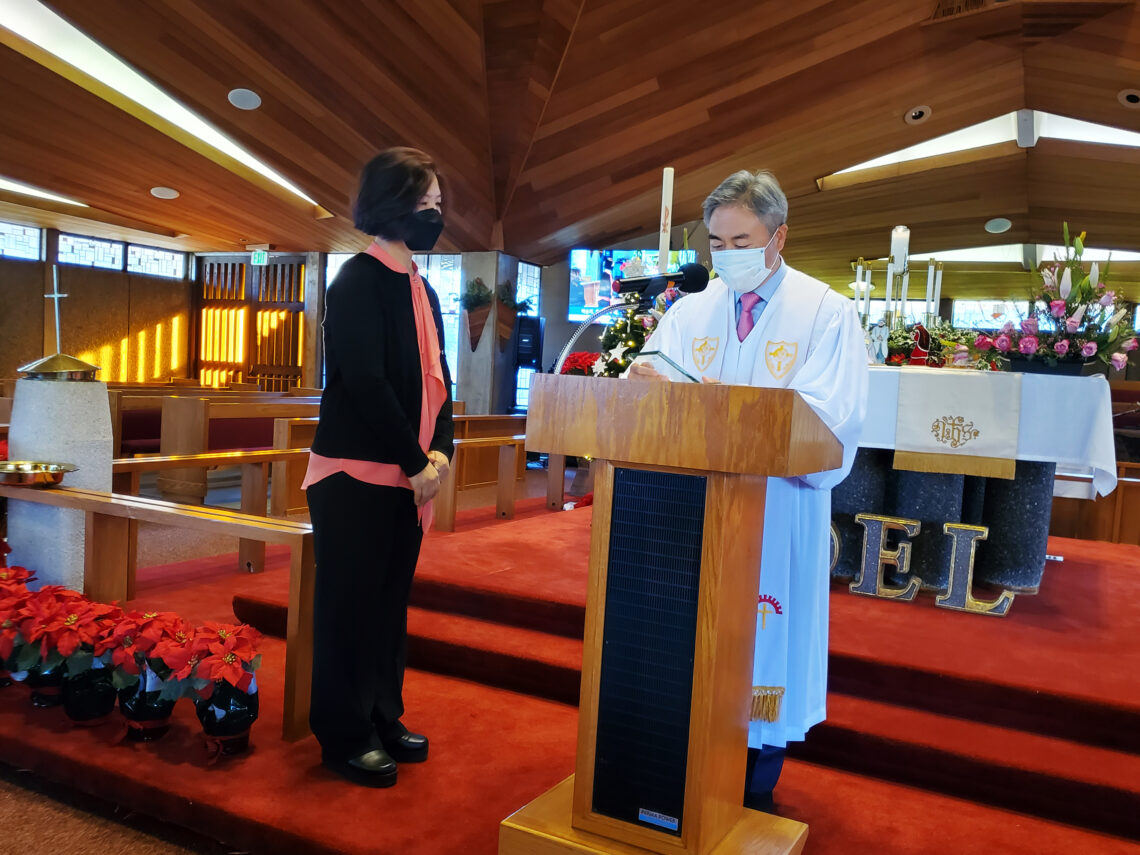 A woman speaks at a podium inside a wooden church sanctuary.