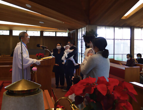 A priest blessing a baby in a church ceremony with family present.