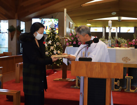 A woman receives a certificate from a priest during a ceremony.