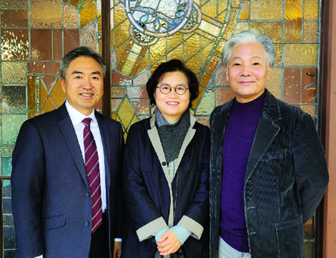 Three people standing together in front of a stained glass window.