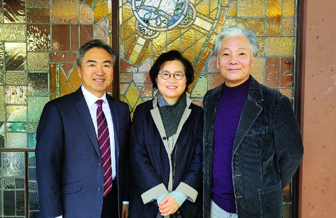 Three people standing together in front of a stained glass window.