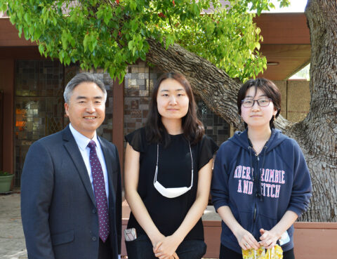Three people posing outdoors with greenery in the background.