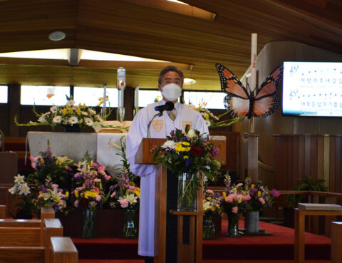 Minister delivering a sermon in a flower-adorned church sanctuary.