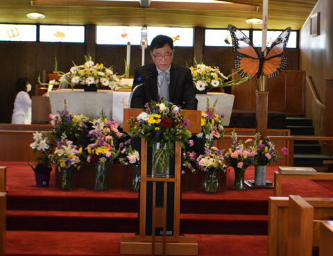 Man speaking at a decorated church podium with floral arrangements.