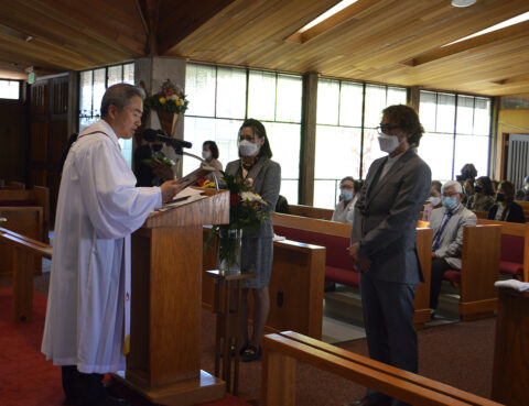 A priest gives a rose to a woman inside a church while another woman watches.