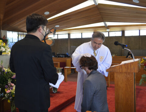 A man in white robes blessing a young boy during a church ceremony.