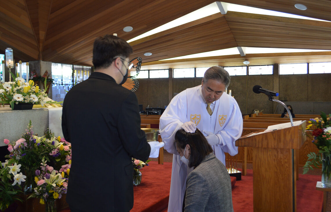 A religious ceremony with a priest blessing a kneeling woman.