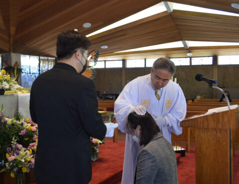A religious ceremony with a priest blessing a kneeling woman.