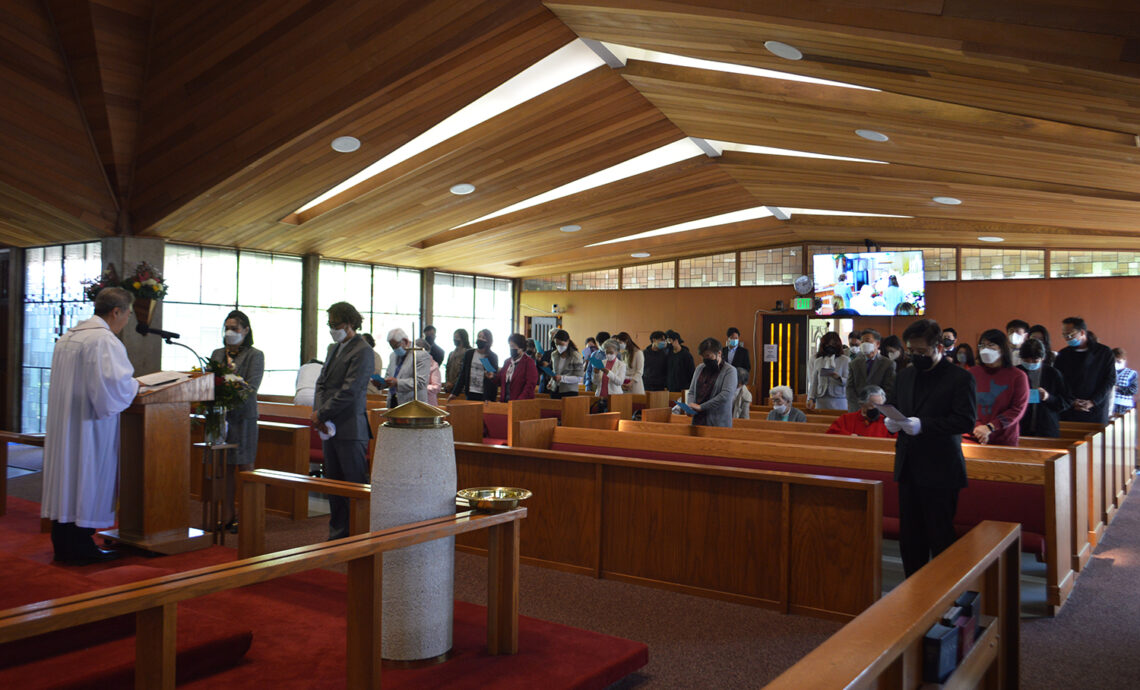 People gathered inside a church with wooden beams and stained glass windows.