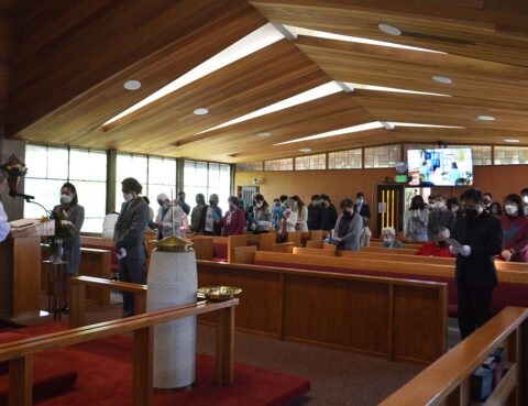 People gathered inside a church with wooden beams and stained glass windows.