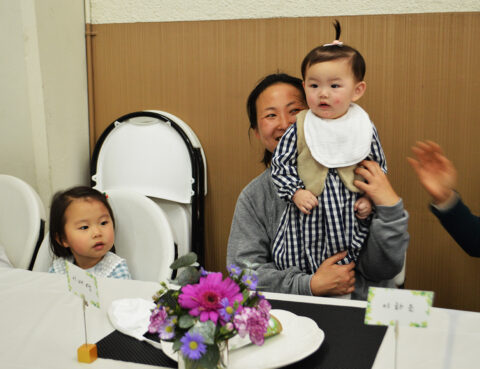 A man holding a baby with a toddler nearby at a table with flowers.