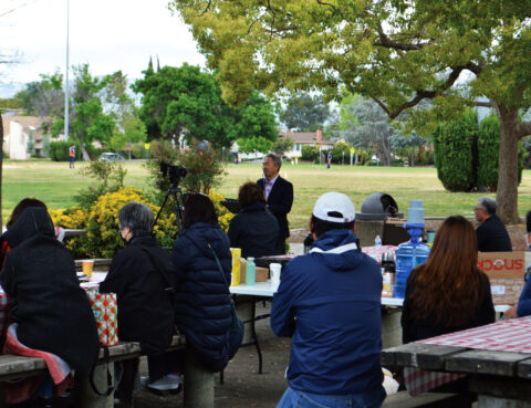 A speaker addresses an outdoor audience at a park.