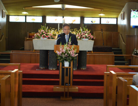 Man speaking at a church podium with floral decorations.