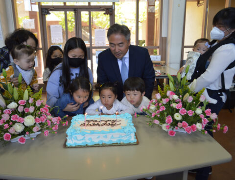 Children and adults gathered around a cake with flowers on the table.
