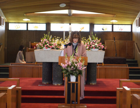 Woman speaking at a floral-adorned podium in a church.