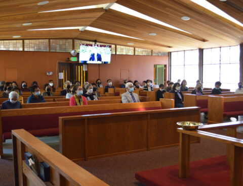 People attending a meeting in a wood-paneled room with a large screen.