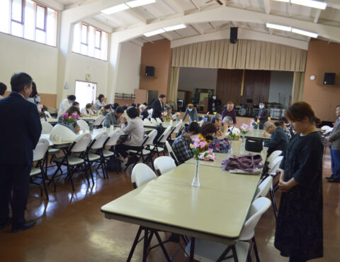 People gathered in a hall for an event with tables and chairs arranged.