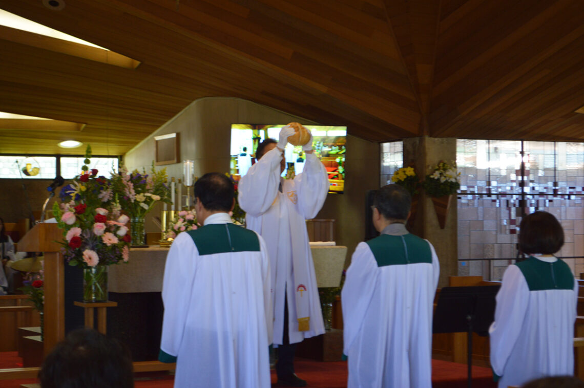A priest holds up the Eucharist during a church service with two altar servers kneeling nearby.