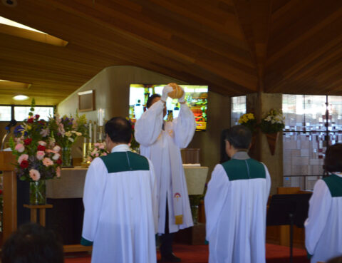 A priest holds up the Eucharist during a church service with two altar servers kneeling nearby.