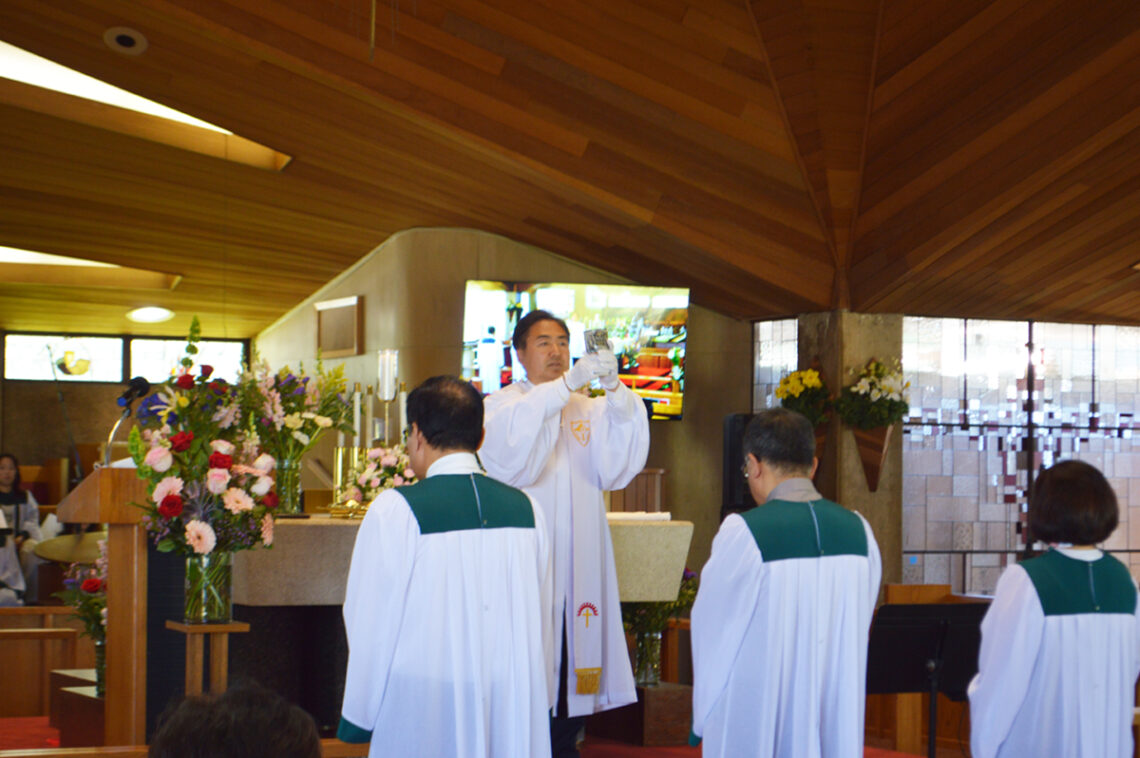 Priest blessing two altar servers in a wooden chapel.