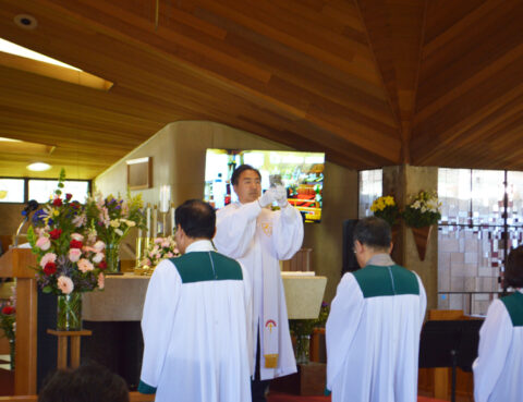 Priest blessing two altar servers in a wooden chapel.