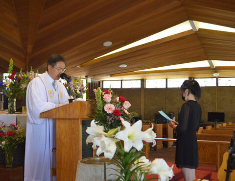 A man speaking at a podium in a church with a woman standing nearby.