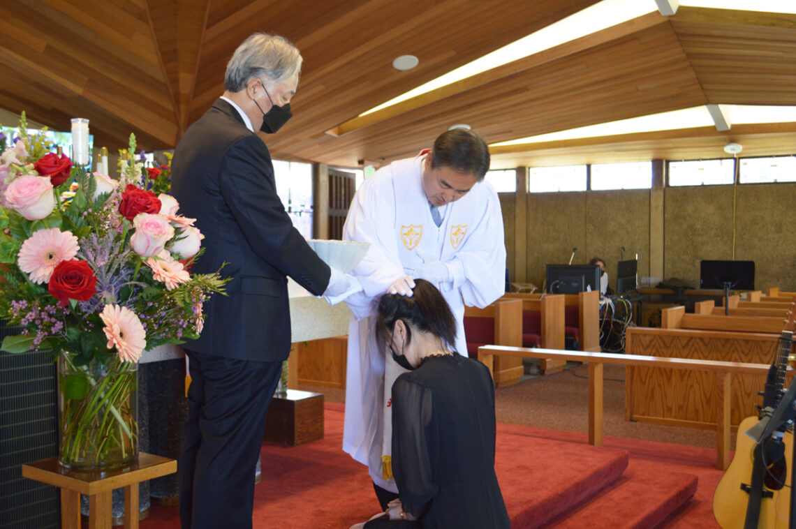 A woman kneels before a man in white in a formal ceremony.