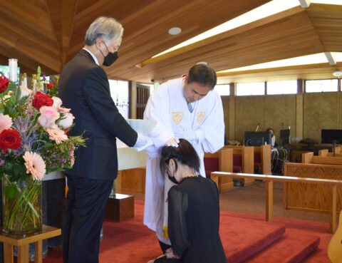 A woman kneels before a man in white in a formal ceremony.
