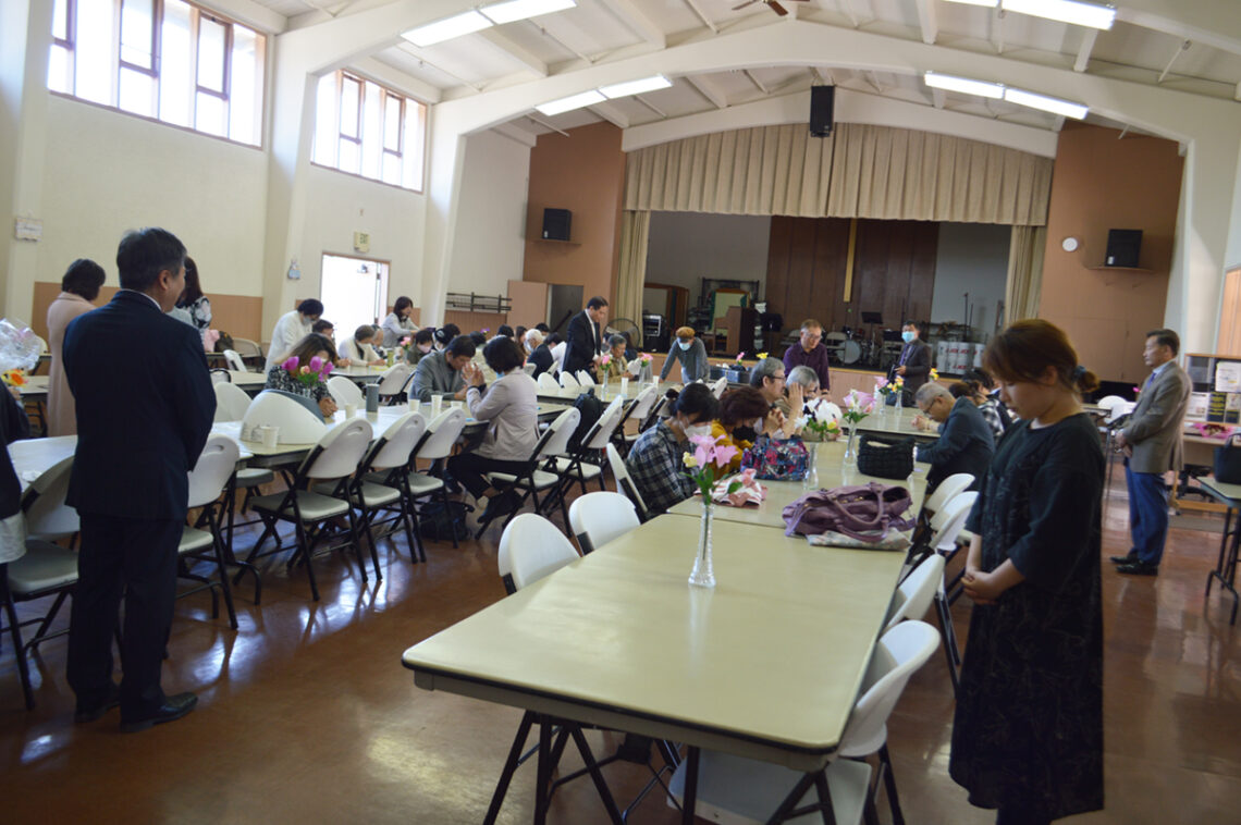 Large indoor event with people seated at long tables in a hall.