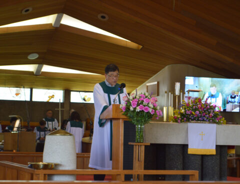 A priest speaking at a church altar decorated with flowers.