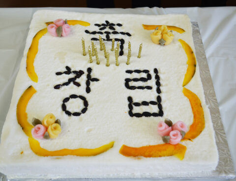A decorated white cake with Korean writing and floral accents.