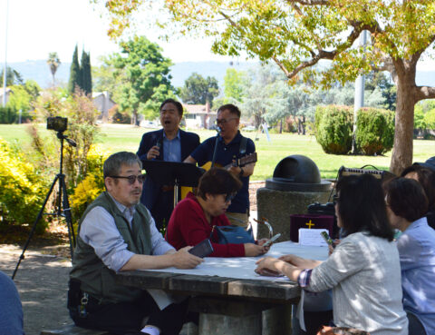 A group of people outdoors working and discussing around a table.