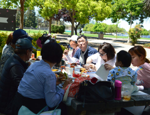A group of friends enjoying a meal together outdoors on a sunny day.