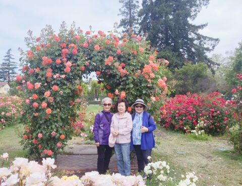 Three people posing under a colorful flower arch in a garden.