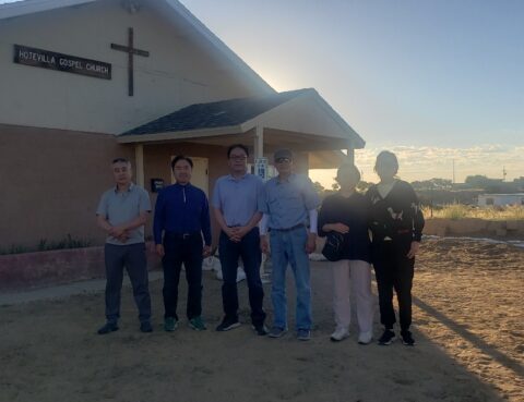 Group of six people standing outside a church at sunset.