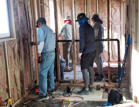 Four workers renovating a room with exposed insulation and framing.