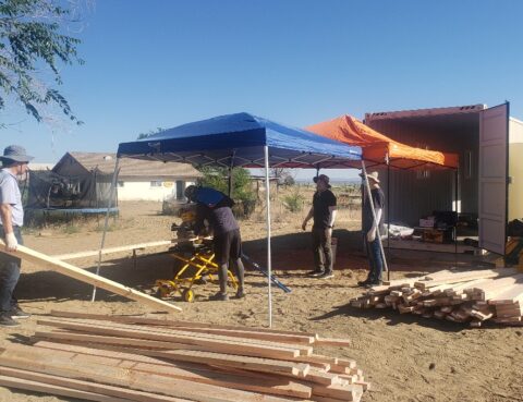 People building a wooden structure under blue and orange canopies.