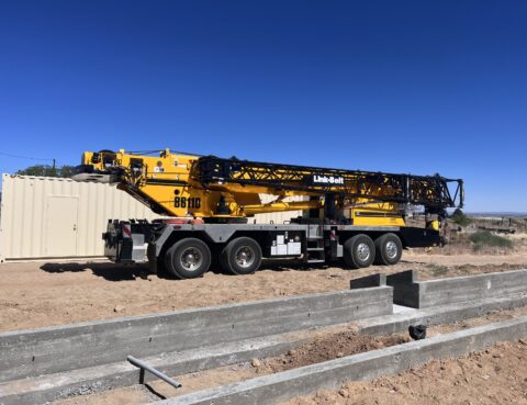 Large yellow crane truck parked at a construction site under a clear blue sky.