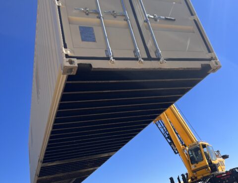 A crane lifting a large shipping container against a clear blue sky.