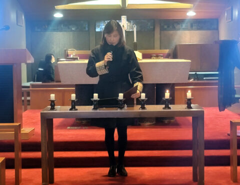 A woman standing behind a wooden table with candles in a dimly lit room.
