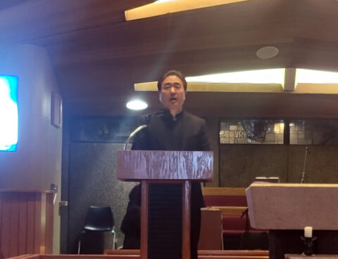 Man speaking at a wooden podium inside a room.
