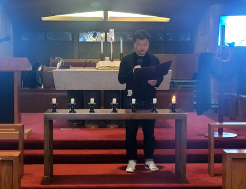 Person standing and reading in a church with candles on the altar.