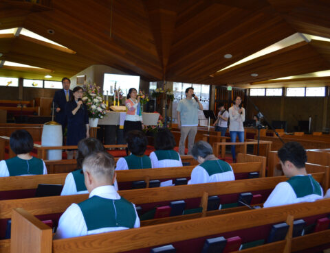 Graduation ceremony with students and speakers in a wooden auditorium.