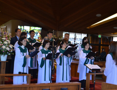Choir members in robes singing inside a wooden church.