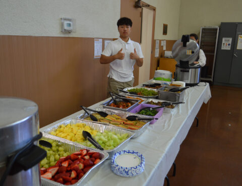 A young man giving thumbs up beside a buffet table with various foods.