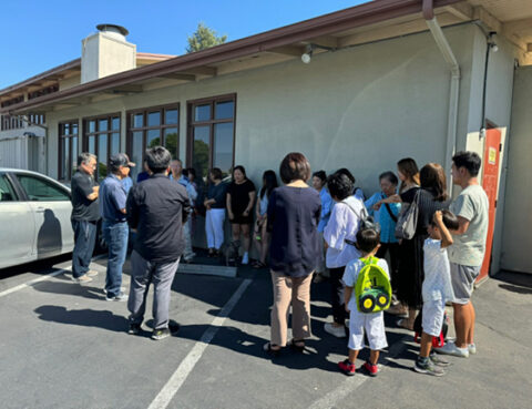 A group of people gathered outside a building on a sunny day.