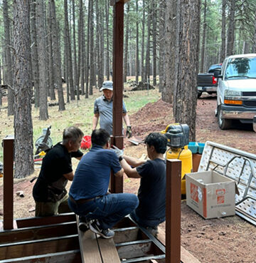 People gathered in a forest clearing with camping gear and a van nearby.